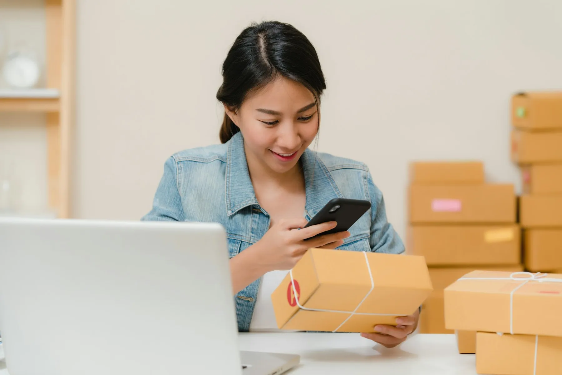 Online seller checking an order on her phone next to packed boxes